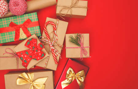 Beautiful Christmas wrapped gifts lie on a red background. The presents are decorated with a Christmas cane, a coniferous branch, shiny, bright festive ribbons and bows.の写真素材