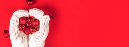 Red Christmas tree toys balls lie in female hands in white mittens. Winter Christmas banner with copy space.の写真素材