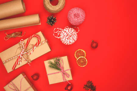 Beautiful Christmas wrapped gifts lie on a red background. The presents are decorated with a Christmas cane, a coniferous branch, shiny, bright festive ribbons and bows.の写真素材