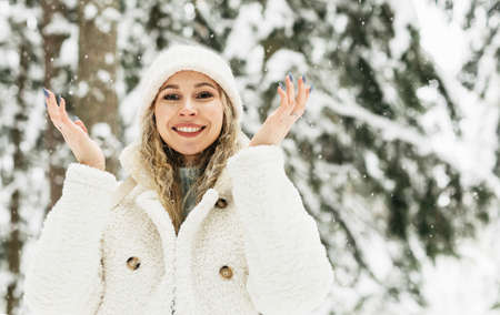 A young girl with a beautiful smile and brown eyes in white clothes catches snowflakes in a snowy forest in the cold in winterの写真素材