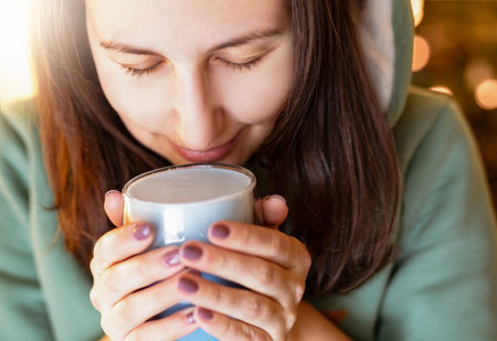 A girl in the rays of the sun drinks warm, warming blue matcha tea.