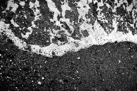 Pebble beach black and white. White foam waves. Shiny bright dark background. Luxury black texture.の写真素材