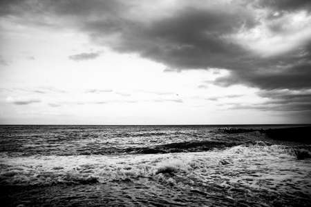 Seascape. Dark pebbles on the beach. White sea waves. Horizon. Natural black and white background.の写真素材
