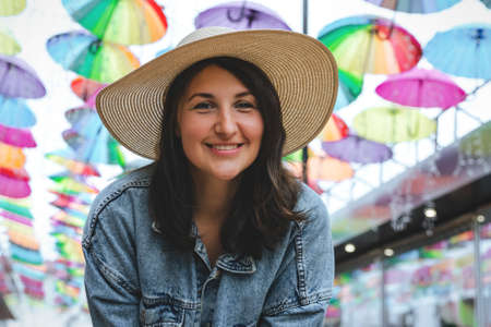 Summer portrait of a beautiful girl in a straw hat on a background of colorful umbrellas.の写真素材