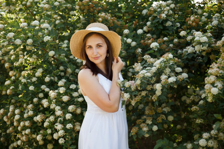 Summer portrait of a beautiful smiling girl in a straw hat on a background of white flowers.の写真素材