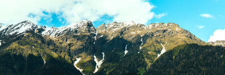 A high mountain against a background of blue sky and white clouds. At the foot of the path, green...
