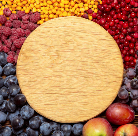 Ripe juicy bright raspberries, sea buckthorn, cranberries, grapes, plums, apples lie around a wooden background. Space for text copy space.の写真素材