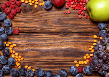 Ripe juicy bright raspberries, sea buckthorn, cranberries, grapes, plums, apples lie on a dark wooden background. A place to copy the text.の写真素材