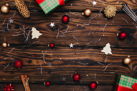 The atmosphere and symbols of Christmas. On the wooden table there are festively packed gifts, decorations, sequins, stars, cones, Christmas trees and red balls of Christmas toys.の写真素材