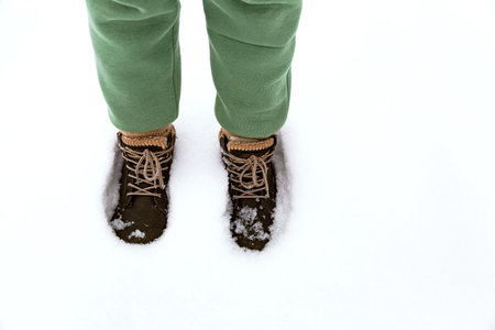 A girl in green warm pants and boots walks forward through deep snow in winter, leaving footprints behind her.の写真素材