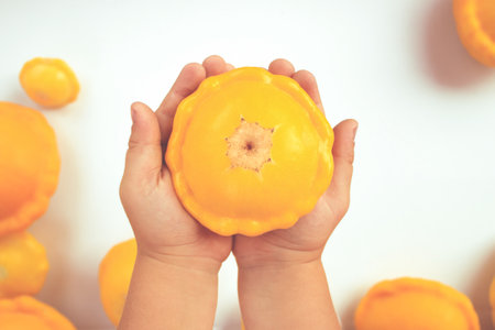 Ripe, bright, yellow patisson in children's hands on the background of a large number of vegetables on a white background.の写真素材