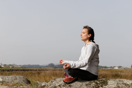 Blonde girl meditating in nature on top of a rock