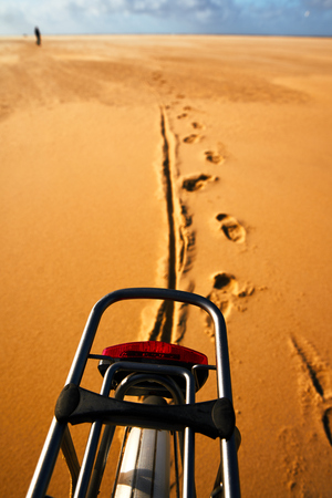 Walk at the beach with a bike at Texel Netherlands. View to the back with footprints in the sand and an unknown person in the background.の写真素材