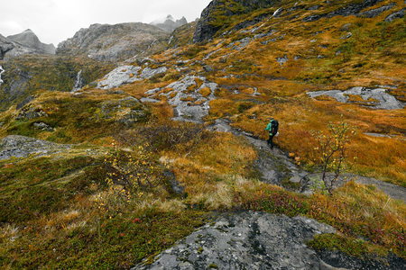 Young man hiking on a rocky trail with backpack in the mountains of the Lofoten in Norway.  The hiker is walking on the path to the summit of the mountain. It is a rainy day in moskenesoy.の写真素材