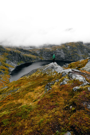 Young man standing at famous cliff edge and enjoying a scenic view over a valley, lake and the...