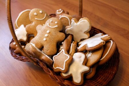 Homemade gingerbread men in the woven basket on the wooden table. Christmas cookies with smiling faces covered with icing. New Year pastry in the shape of stars and men. Festive winter backgroundの写真素材