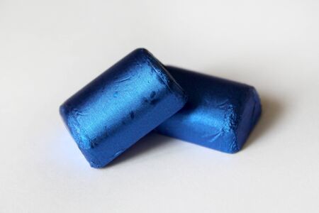 A pile of chocolate candies wrapped in blue foil isolated on white surface. Template for greeting card, poster or invitation. Sweets scattered on the white smooth table. Backdrop or backgroundの写真素材