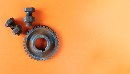 Rusty bolts, nuts and gear wheel made of chocolate isolated on orange background. Mechanic gearing...