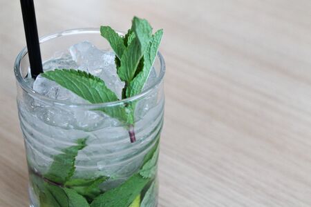 Glass of mochito cocktail on wooden table with black straw, ice and mint leaf. Copy space for text. Alcoholic or nonalcoholic and soft drink in the bar or restaurant or cafe. Picture for menu, invitationの写真素材