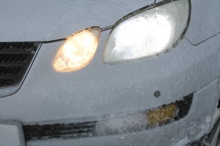 Car headlights covered with frost and slush snow during winter blizzard. Bad and extreme weather conditions background. Northern seasonal backdropの写真素材
