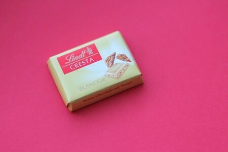 Magadan, Russia - January, 2020. Lindt cresta white chocolate wrapped in yellow paper. Famous candy isolated on red background. Copyspace for text. Company name and logoのeditorial素材