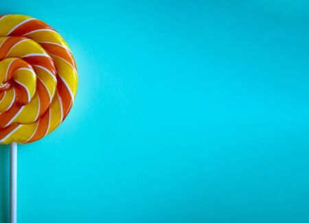 Bright blue background with half swirl lollipop with copy space. Festive backdrop with colorful twisted candy. Rainbow round sweet on stick. Template for banner, poster, greeting card, web siteの写真素材