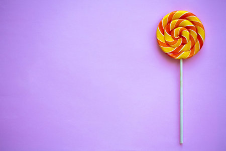 Bright swirl lollipop on purple background with copy space. Festive background with colorful twisted...