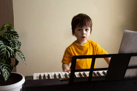 A boy playing the synthesizer. Toddler learning how to play piano. Child looking at the camera. Early development and education conceptの写真素材