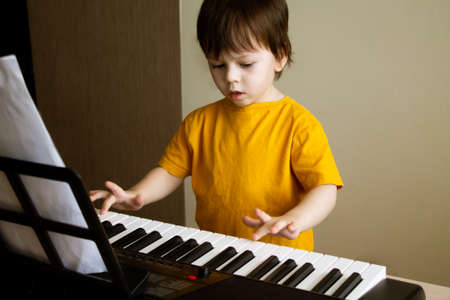 A boy playing the synthesizer. Toddler learning how to play piano. Childs hands on the keyboard. Early development and education conceptの写真素材