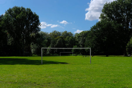 Two football or soccer goalposts in parallel in a park with green grass and blue skies and people...
