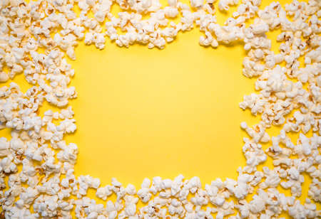 A pile of white salty popcorn, scattered on a yellow background, leaving a square space in the middleの写真素材