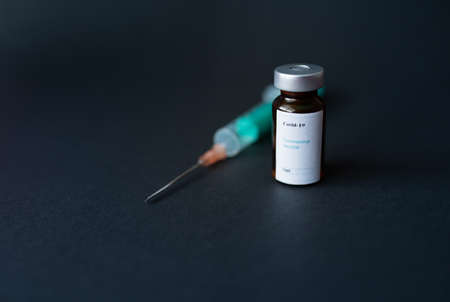 A vial of coronavirus vaccine, a syringe with a needle, with a black background.の写真素材