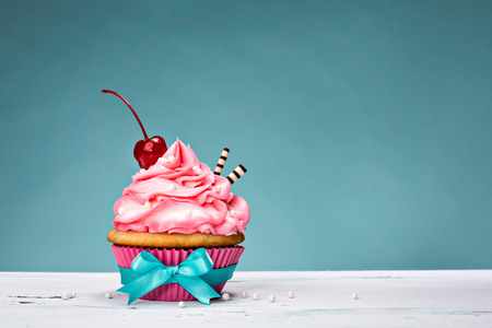 Cupcake with pink buttercream icing and a cherry on top.