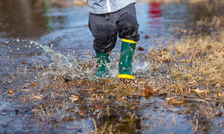 Very wet little boy running through puddles in the grass wearing rainboots.の写真素材