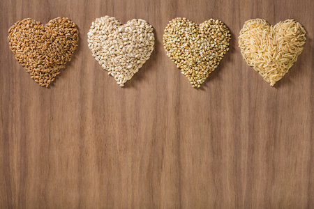 Healthy whole grains shaped like hearts over a wooden background. Wheat, barley, buckwheat and brown rice.の写真素材