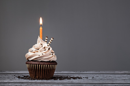 Chocolate Birthday cupcake with  buttercream icing and orange candle over a grey background.の写真素材