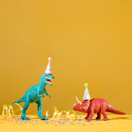 Two dinosaurs with birthday hats partying on a yellow background.の写真素材