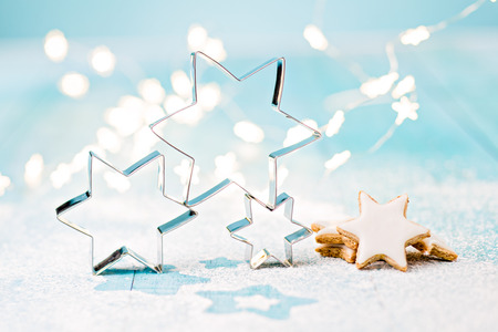 Star cookie cutters and cinnamon cookies on blue boards sprinkled with powdered sugar and soft, out of focus, star shaped christmas lights.の写真素材