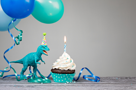 Blue Dinosaur toy with birthday cupcake and balloons on a gray background.の写真素材
