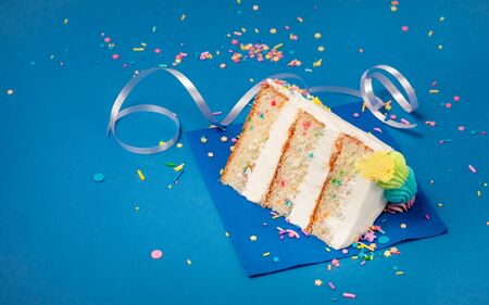 Slice of confetti Birthday cake   with buttercream icing and Sprinkles over a blueの写真素材