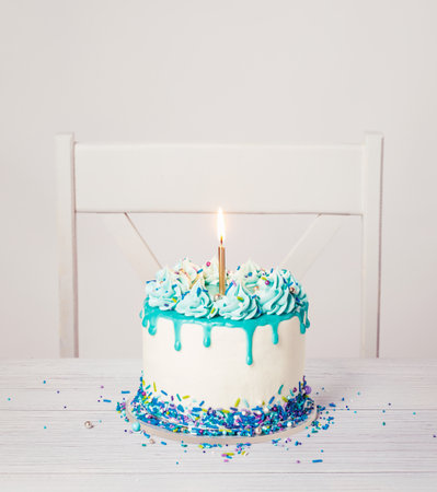 Birthday Cake with blue icing, ganache drip, sprinkles, and lit candle on a white backgroundの写真素材