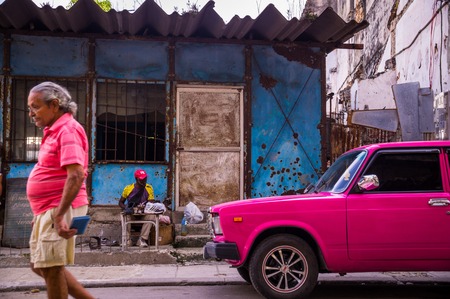 Havana, Cuba on December 23, 2015: A man walks down a street in Centro Habana with his shirt matching the color of a pink oldtimerのeditorial素材