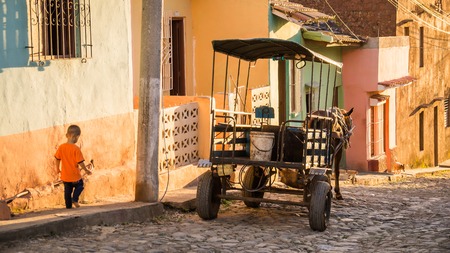 Trinidad, Cuba on December 29, 2015: In late afternoon light a horse carriage is waiting for passengers in front of colorful buildings in Trinidad. Meanwhile a young boy is walking down the sideway.のeditorial素材