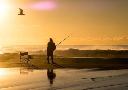 Fishermen with fishing rod at sunrise on beachの写真素材