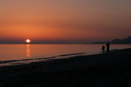 Silhouette of couple walking and posing along the beach at sunsetの写真素材