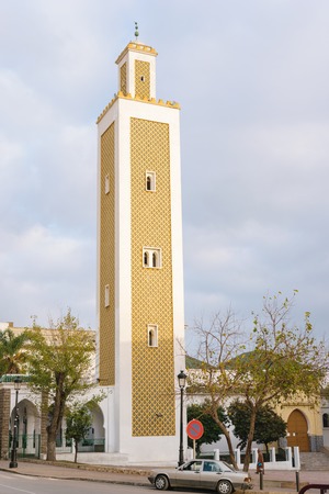A golden Mosque and minaret in Tetouan, Morocco. In front of the Mosque a man in traditional clothing walks by.の写真素材
