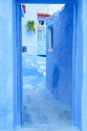 A blue colored and painted doorway in the centre of Chefchaouen, Morocco. In the small window in the background is a cat and watching towards the entrance.の写真素材