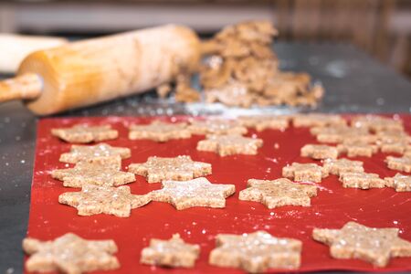 Star shaped cinnamon christmas cookies are ready for the oven and in the background is the cookie dough and a dough roll.の写真素材
