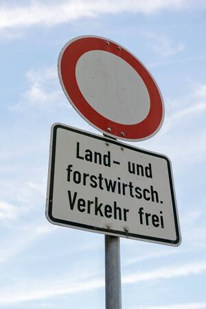 A road sign that says - No thoroughfare - except agricultural and silvicultural traffic in german language in front of blue sky.の写真素材