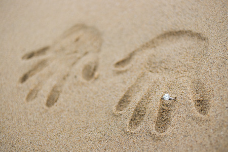 Engagement ring with handprint in sandの写真素材